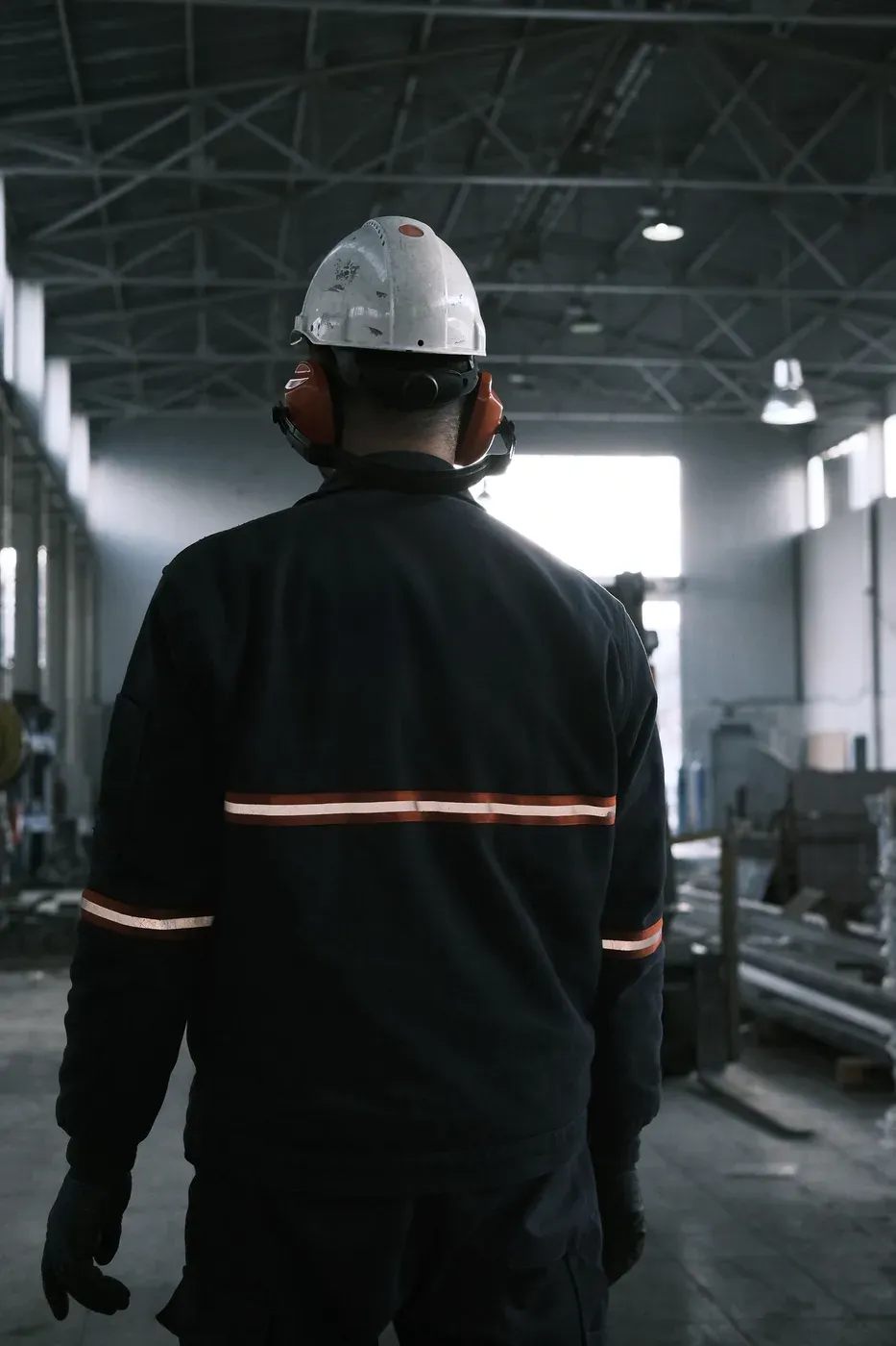 A worker in protective equipment on a factory floor, seen from behind