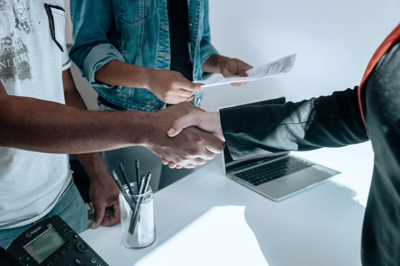 A business handshake over documents and a laptop